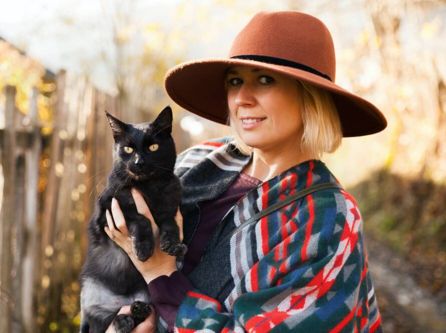 Black cat and stylish traveling woman wearing authentic boho chic style poncho and hat
