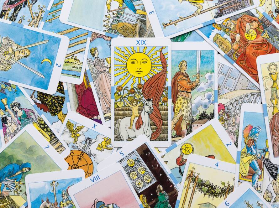 Scattered on the table are tarot cards and a card with an arcana Sun