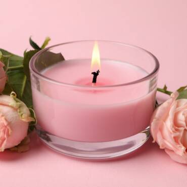 Scented candle and roses on pink background