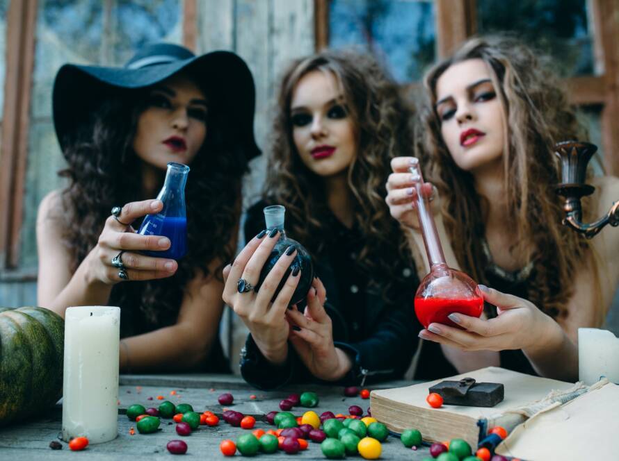 Image of three witches in a dimly lit room surrounded by bottles of magic potions