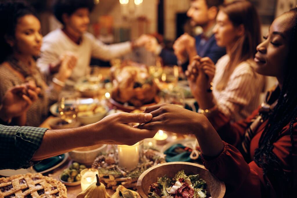 Couple Holding Hands and Giving Thanks During Thanksgiving Dinner with Friends