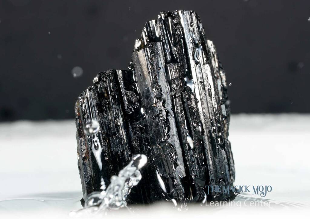 Black tourmaline crystal with water droplets against a dark background.