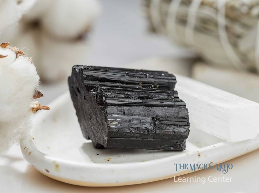 Black tourmaline crystal on a white ceramic plate with cotton and selenite in the background