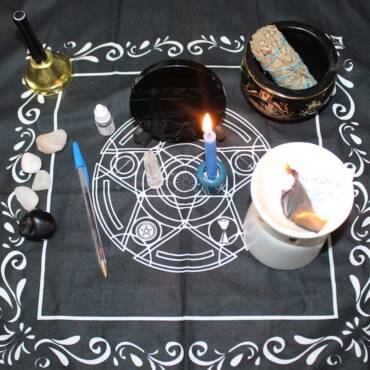 Setup for a Truth Revealing Spell featuring a blue candle, a mirror, clear quartz, a pen, sage, and other magical tools arranged on a mystical black cloth with white symbols.