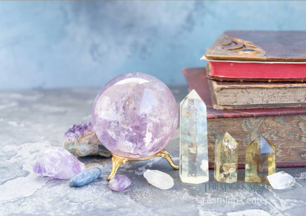 n assortment of crystals including a large amethyst sphere, several clear quartz points, and tumbled stones on a table with vintage books in the background.