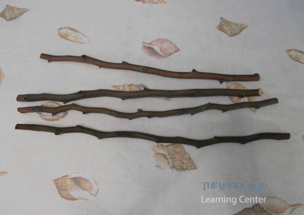Collection of raw wooden sticks laid out on a seashell-patterned fabric, intended for crafting magic wands at The Magick Mojo Learning Center.