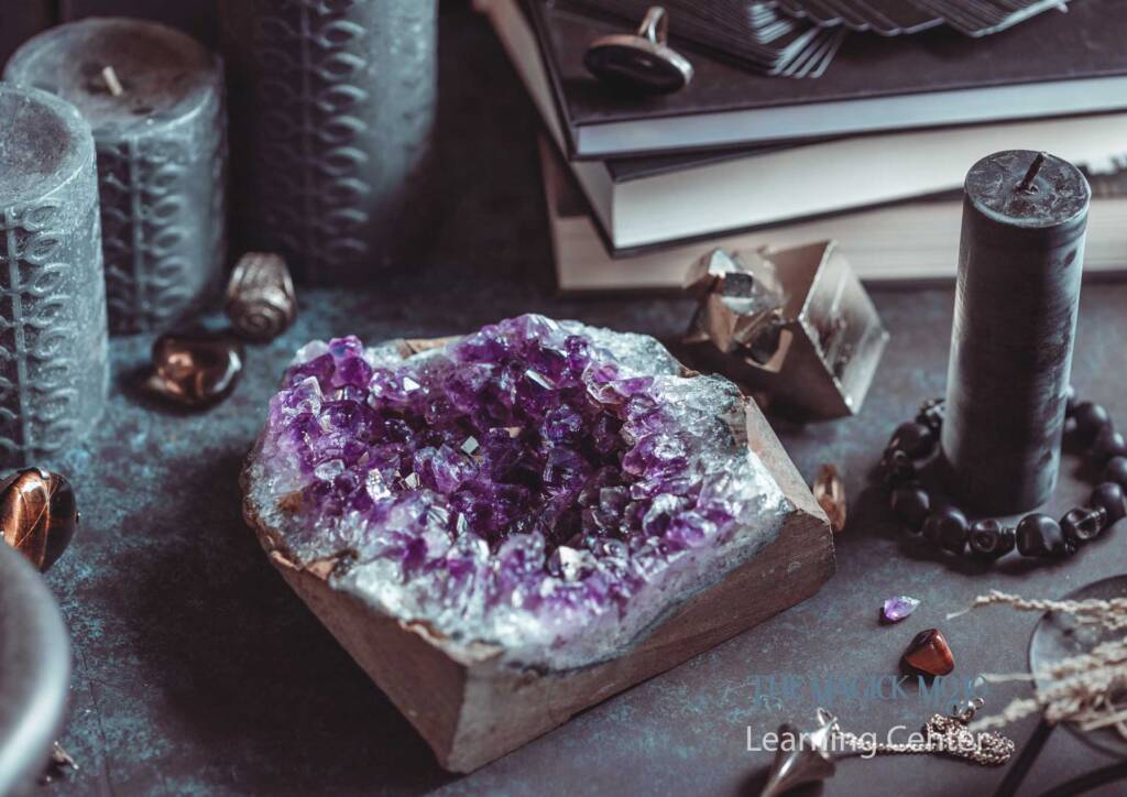 Amethyst cluster surrounded by candles, books, and mystical objects